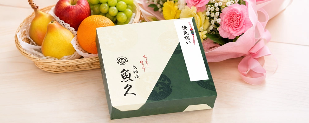 快気祝いの贈り物として、お見舞いの果物と花を背景にした魚久の京粕漬の箱